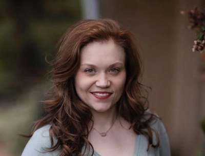 Headshot of chiropractor Lauran Click with long, wavy hair, wearing a light-colored top and photographed outdoors.